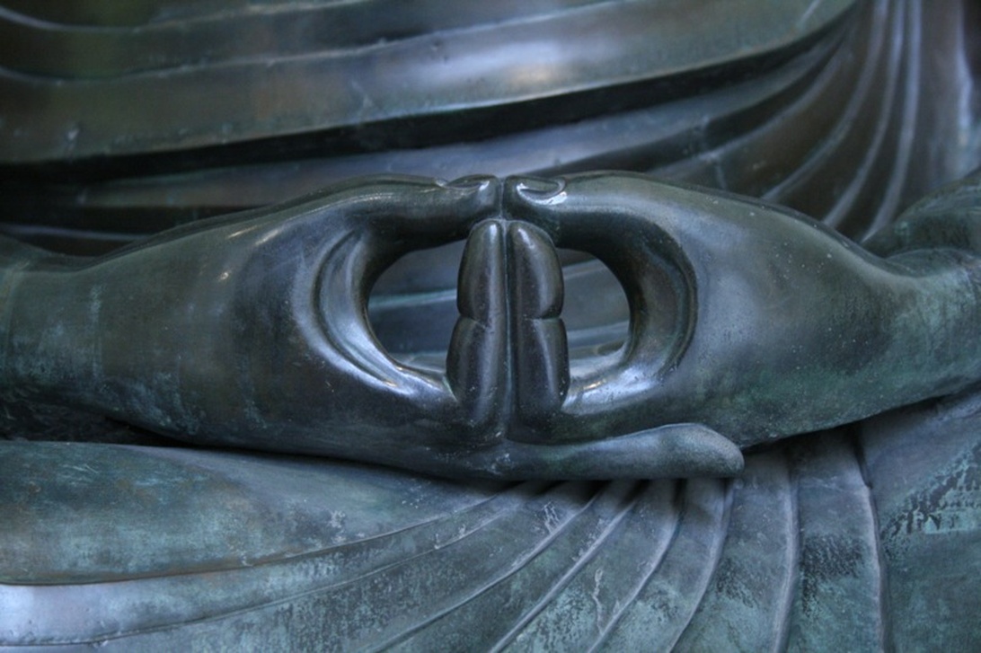 Närbild på en Buddha-statys händer i dhyana mudra, den klassiska meditationsgesten som symboliserar stillhet och koncentration.